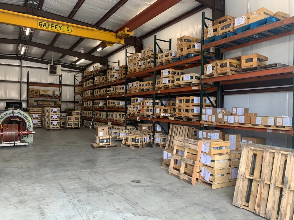 The Capitol Electric warehouse: a yellow five ton bridge crane above steel pallet racking of crated motors, with a stator on the floor